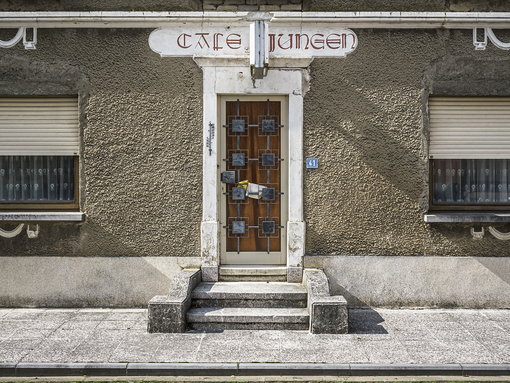 Ancien 'Café Jungen' à Kahler. La façade montre une porte fermée et les volets baissés, témoignant de l'absence d'activité et de l'abandon du lieu.