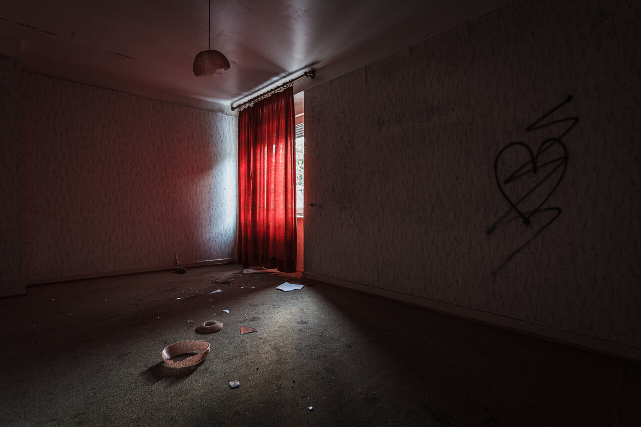 Pièce sombre aux rideaux rouge, au liminaire cassé et aux murs taggés d'un coeur barré...