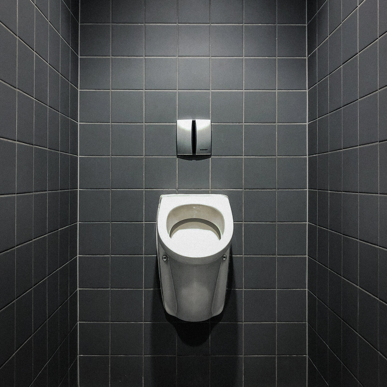 Un urinoir adossé à un mur de carrelages gris antracites...