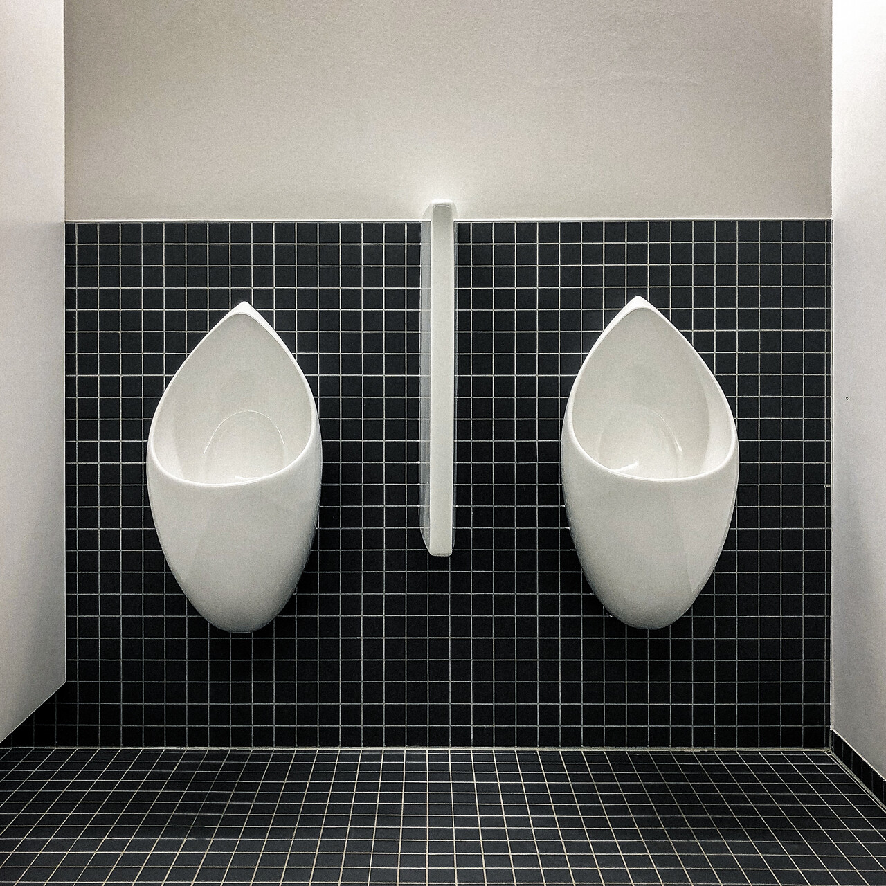 Deux urinoirs en faïence blanche adossés à un mur de carreaux noirs...