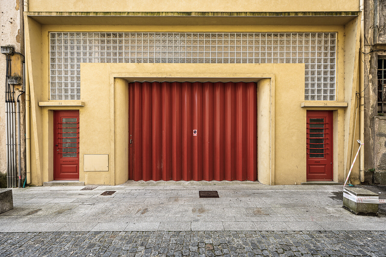 Façade ocre à Vila Nova de Gaia, avec une grande porte industrielle rouge plissée et deux portes latérales.