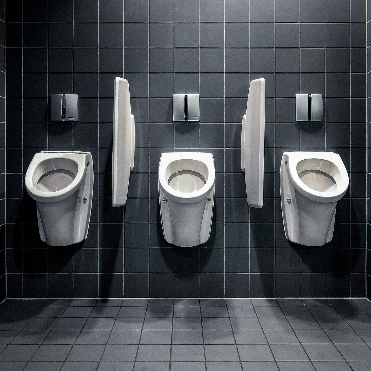 Trois urinoirs adossés à un mur de carelages antracites