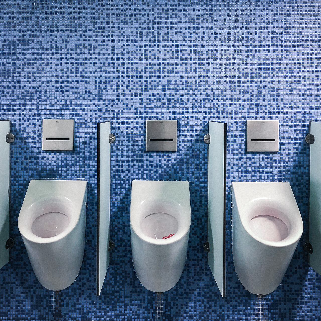 Trois urinoirs adossés à un mur en mosaïque bleue