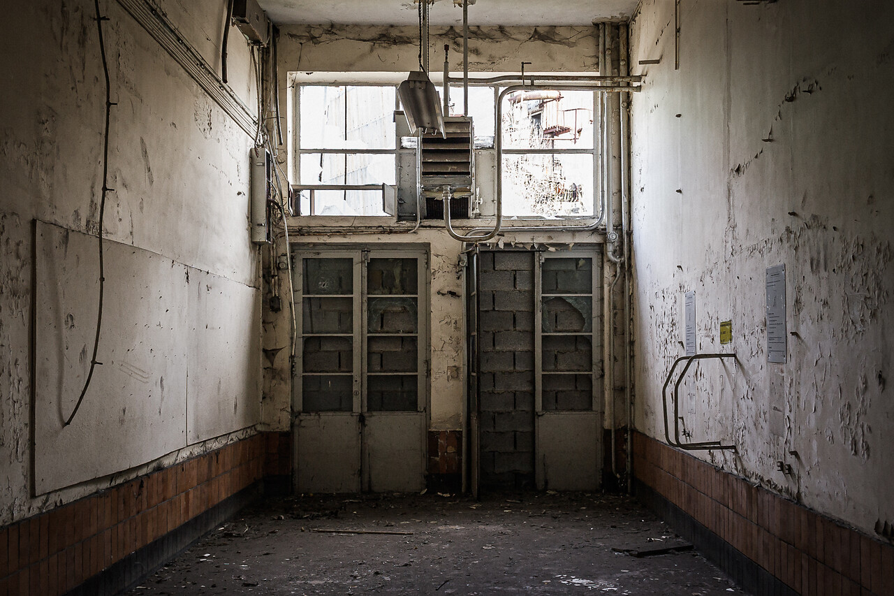 Hall aux murs décrépi donnant sur deux portes murées.