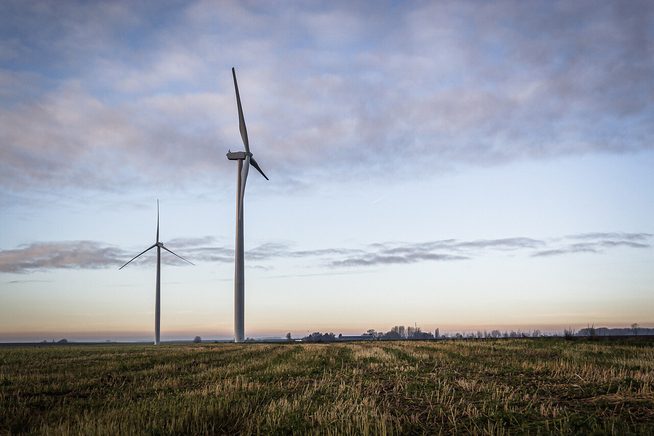 Paysage avec deux éoliennes modernes dans un champ coupé à Sombreffe, Belgique, au crépuscule. Le ciel est nuageux avec des teintes chaudes du coucher de soleil.