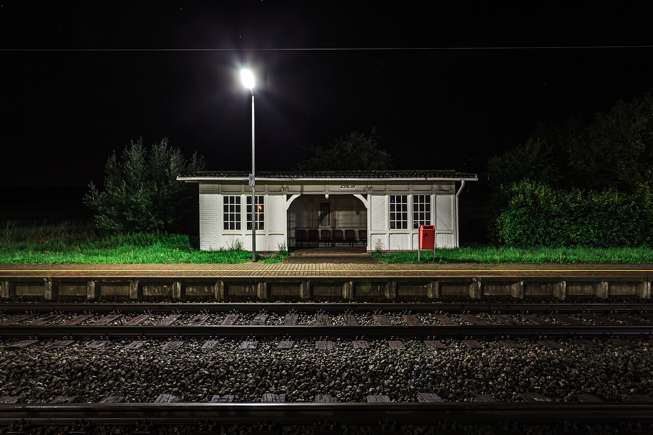 Vue nocturne de face du quai de la gare de Betzdorf, illuminé par un lampadaire puissant au premier plan face aux voies ferrées.