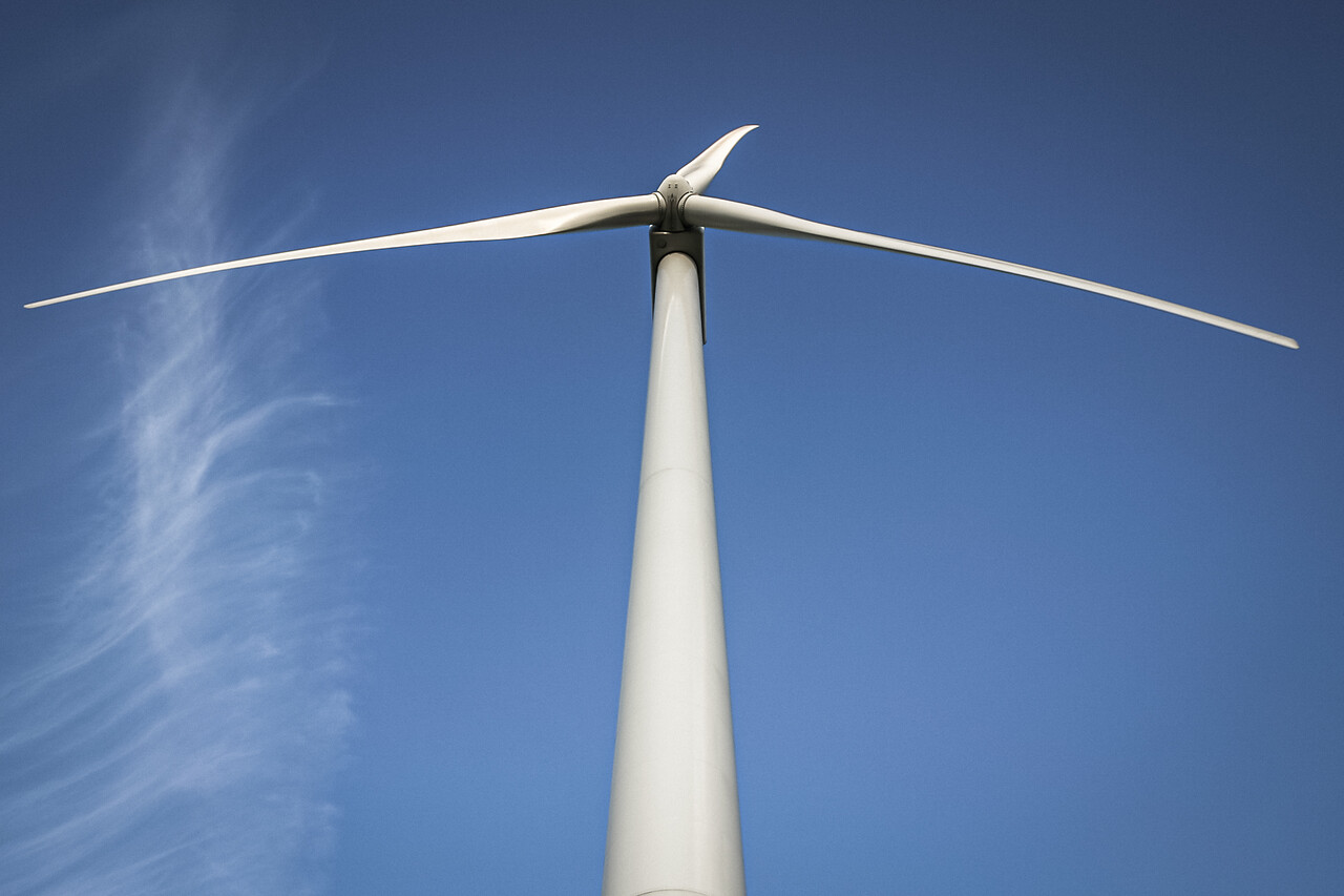 contre-plongée d'une éolienne moderne avec trois pales blanches, se détachant sur un ciel bleu clair avec de légers nuages blancs. Sombreffe, Belgique