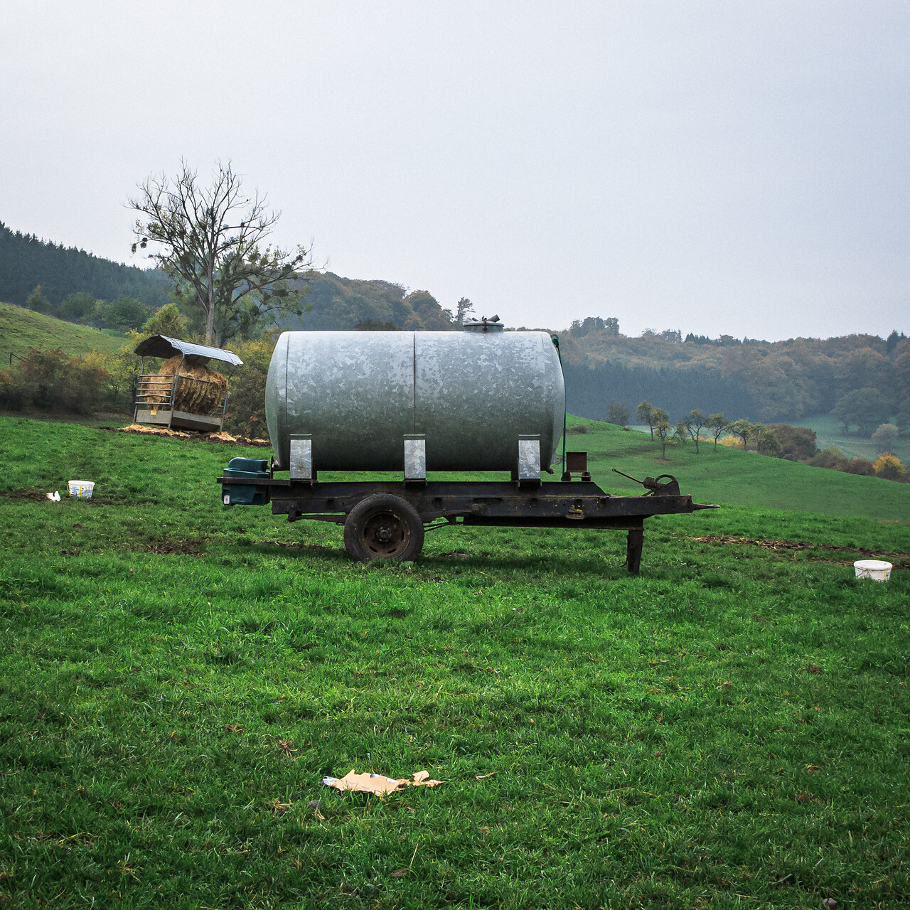 Réservoir métallique sur remorque dans un paysage rural, avec cabane en bois et collines verdoyantes