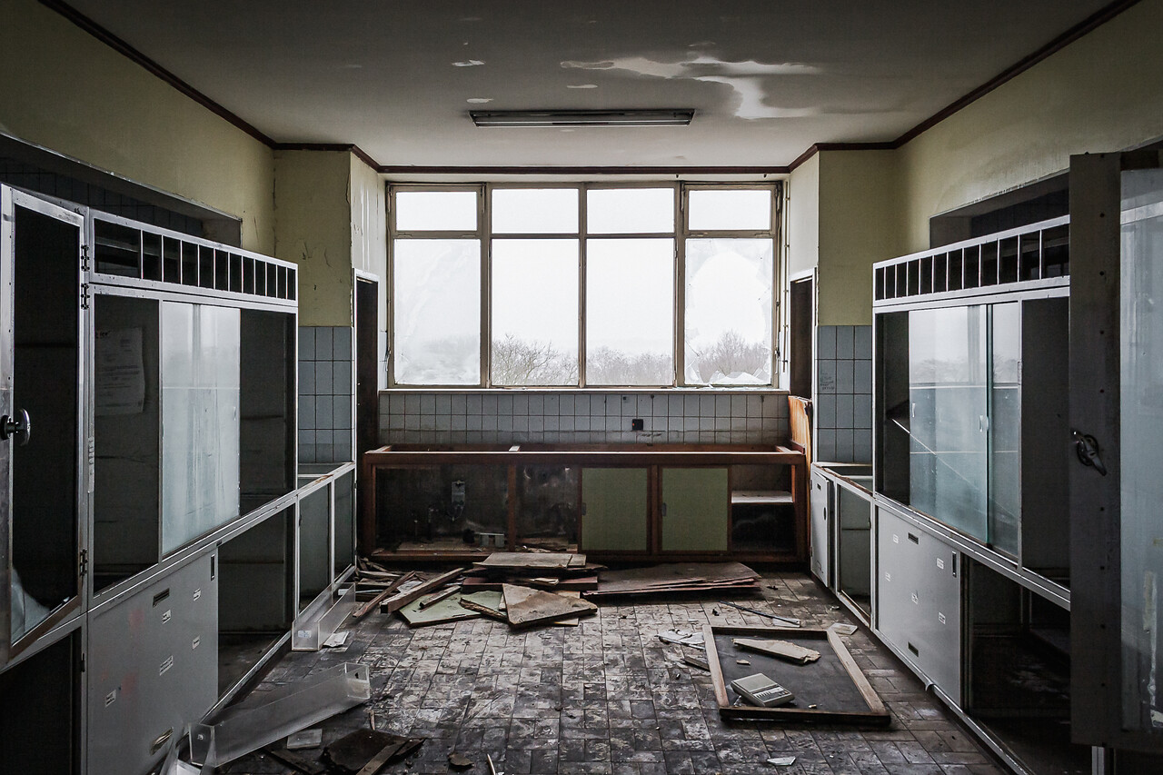 Un laboratoire dans un hôpital abandonné, avec des fenêtres brisées, des meubles en désordre et des débris au sol.
