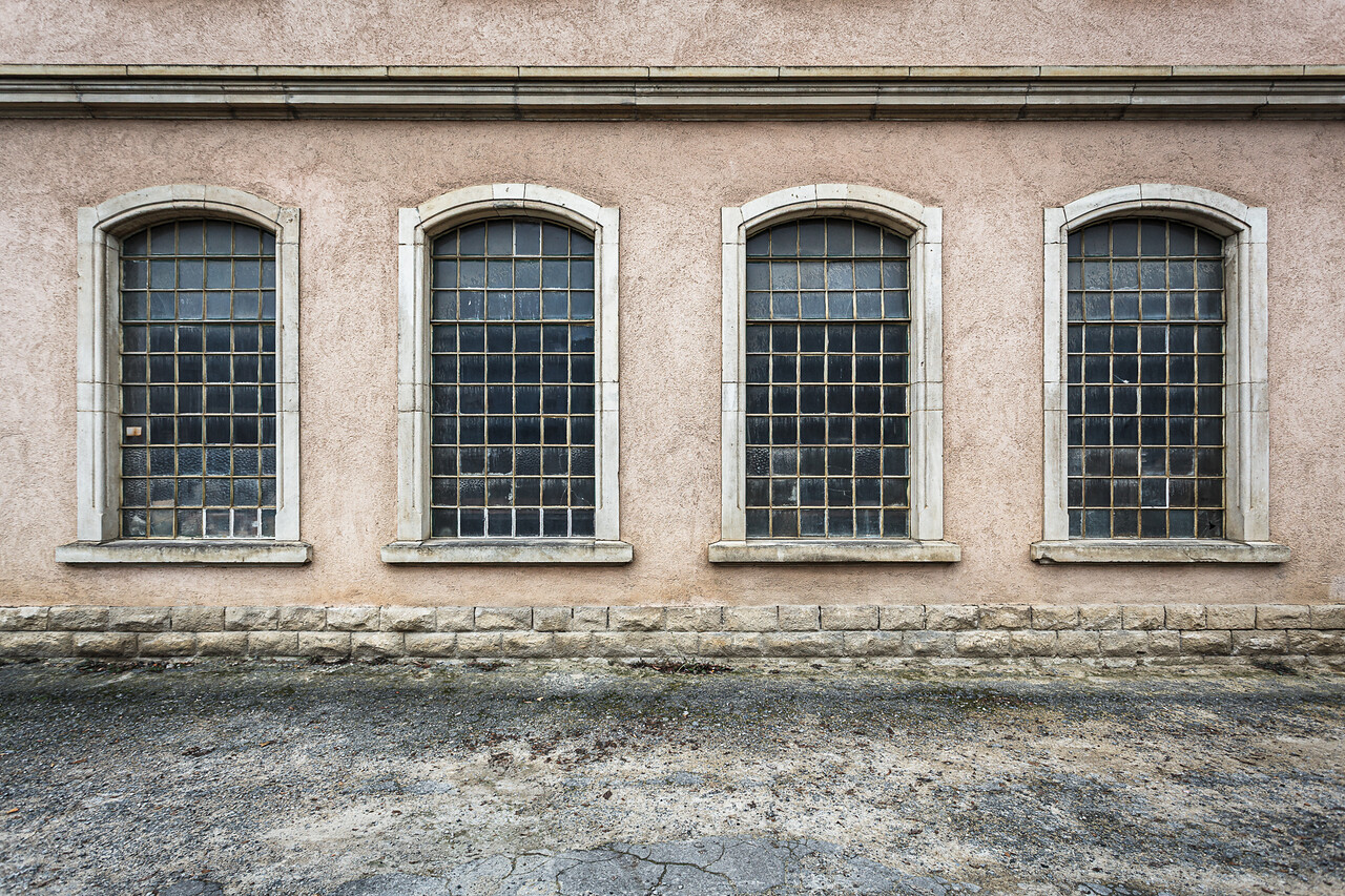Façade industrielle avec de grandes fenêtres à croisillions et des carreaux sales.