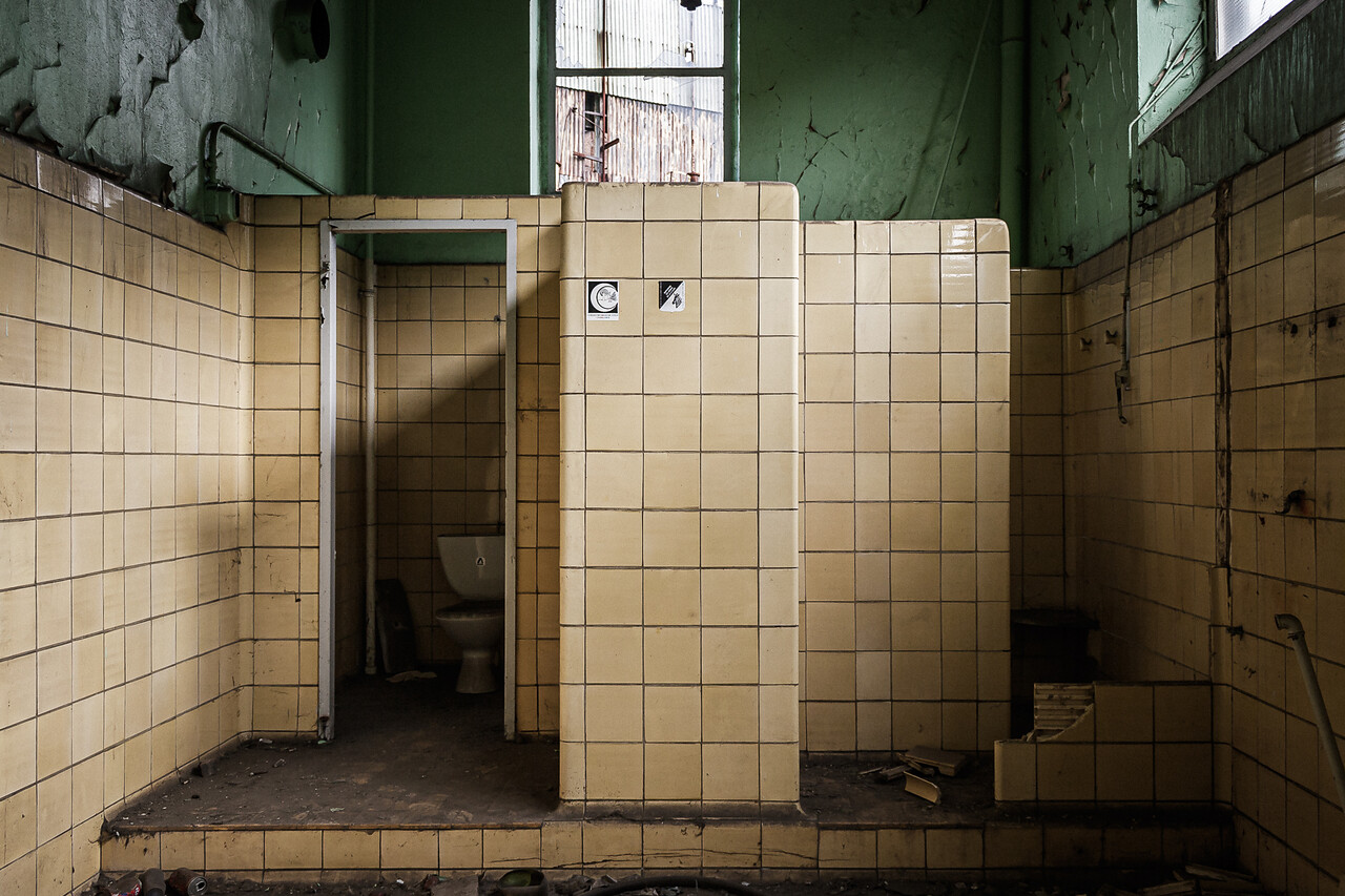Anciennes toilettes couverte de carrelages jaunes dans une usine abandonnée.