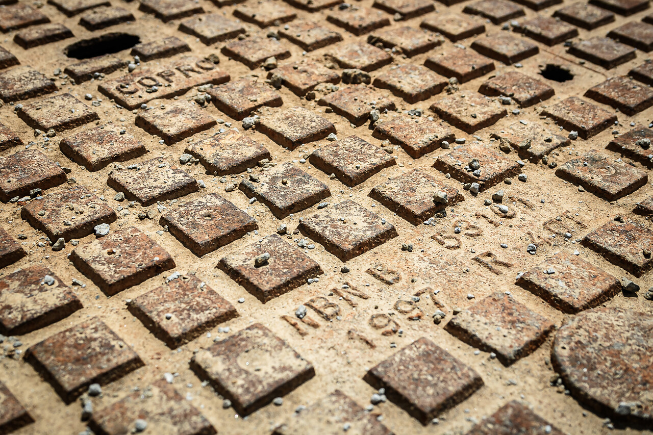 Gros plan d'une plaque d'égout en fonte rouillée avec des motifs carrés en relief et les inscriptions de la marque 'COPRO' et la référence 'NBN B 53101 - 1997 R 40T' à Gosselies en Belgique.