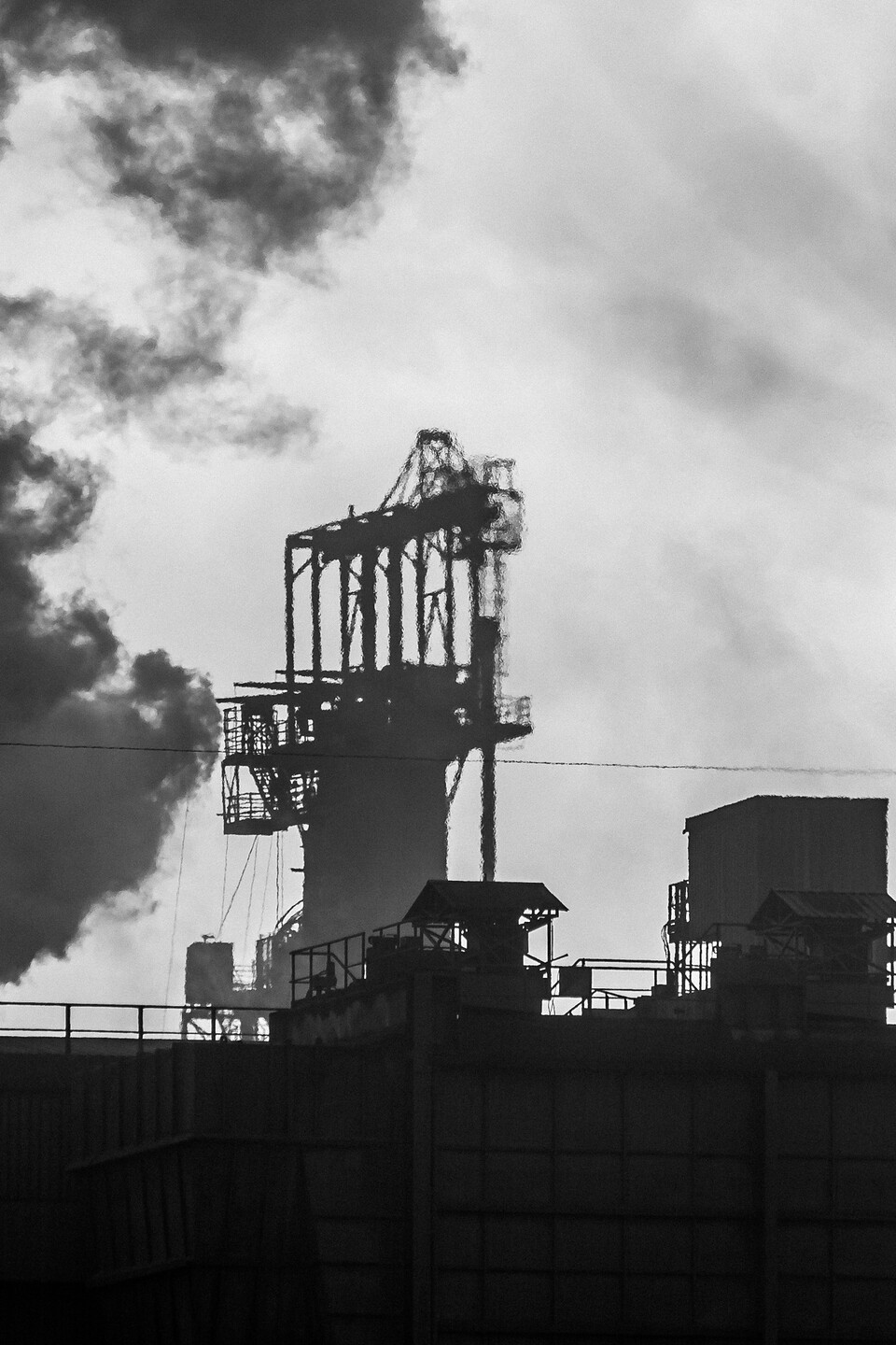 Photographie noir et blanc d'un paysage industriel à Dampremy en Belgique, montrant des structures métalliques complexes, des bâtiments industriels et de la fumée noire s'élevant dans un ciel nuageux.