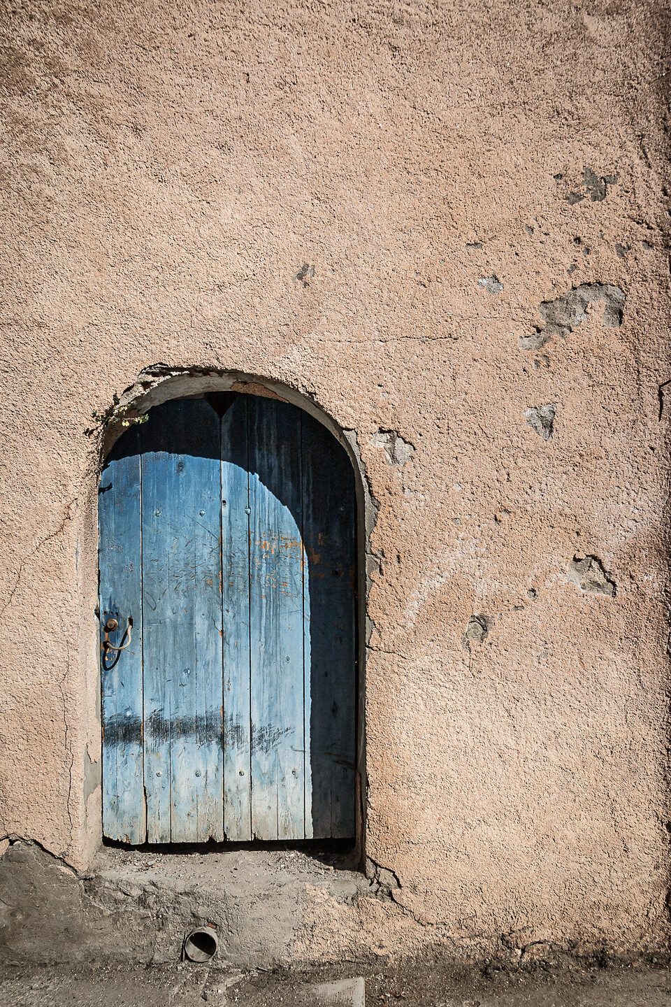 Une vieille porte en bois bleu, usée et écaillée, encastrée dans un mur en stuc orangé avec des fissures et des éclats, ajoutant du caractère à la scène.