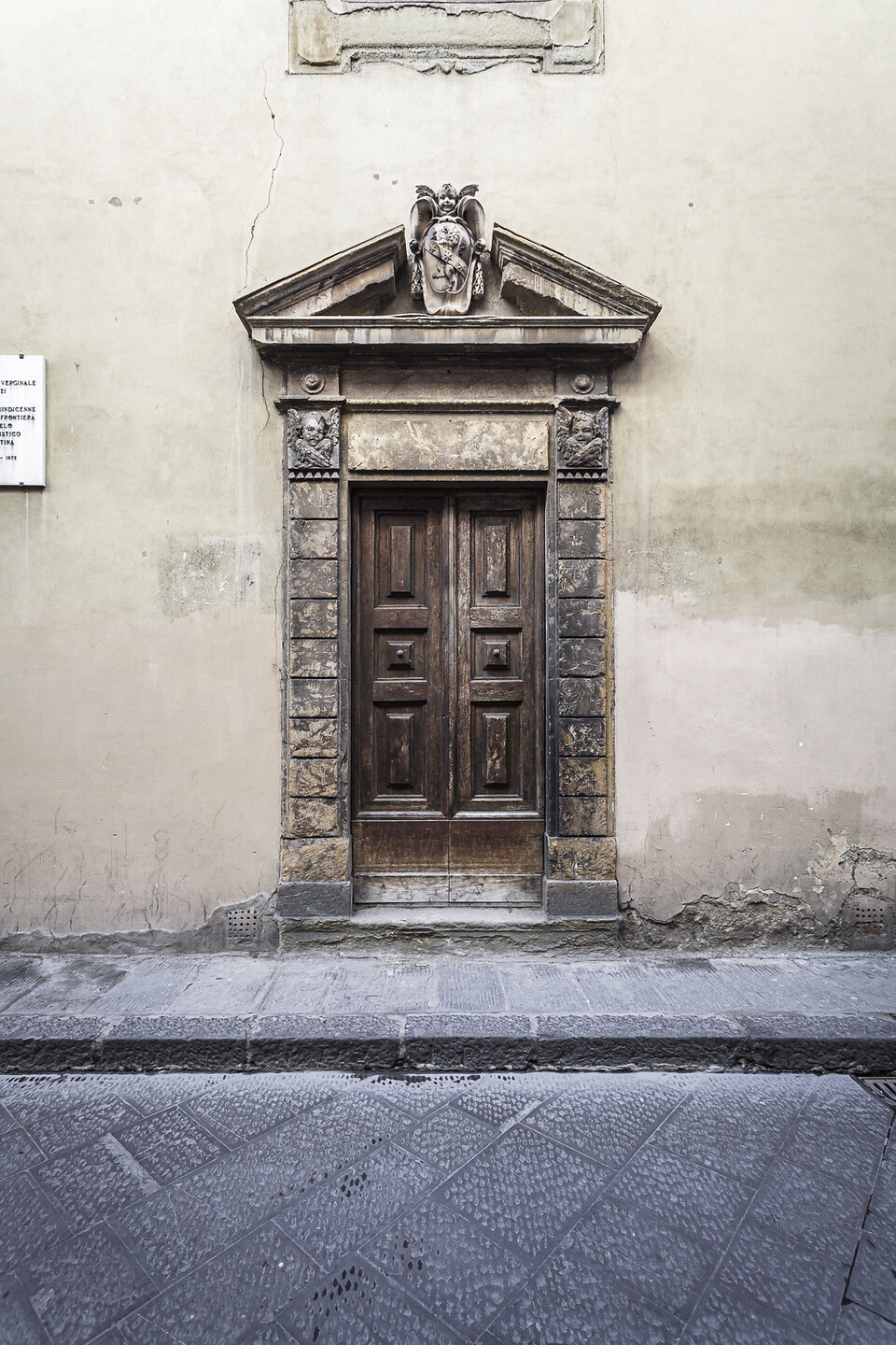 Grand angle sur une porte surmontée de chérubins dans une rue étroite de Florence
