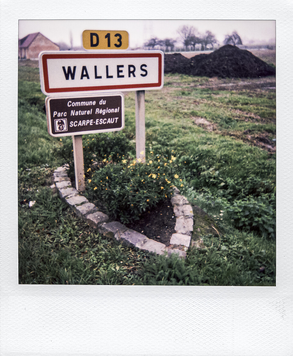 Polaroid montrant un panneau routier blanc bordé de rouge indiquant 'WALLERS', surmonté du cartouche jaune D13, situé dans un paysage rural.