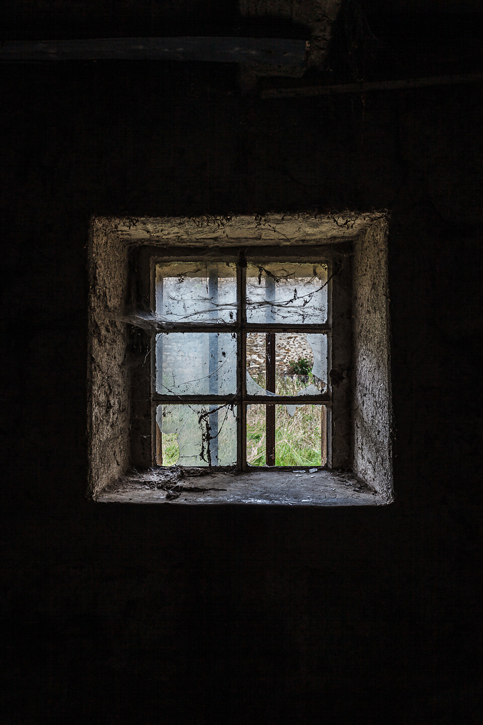 Fenêtre à barreaux et croisillons, ses vitres brisées couvertes de toiles d'araignées....