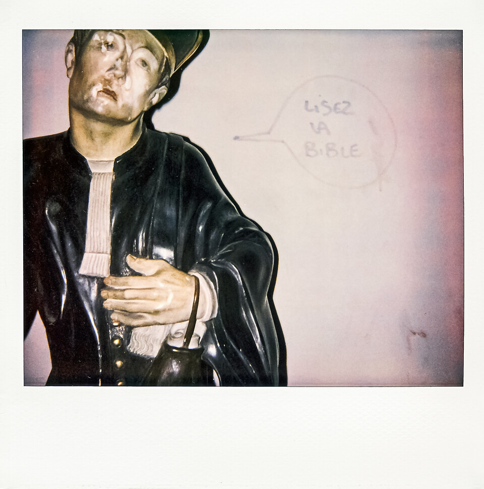 Polarroid d’une statue religieuse adossée à un mur tagué d'un phylactère...