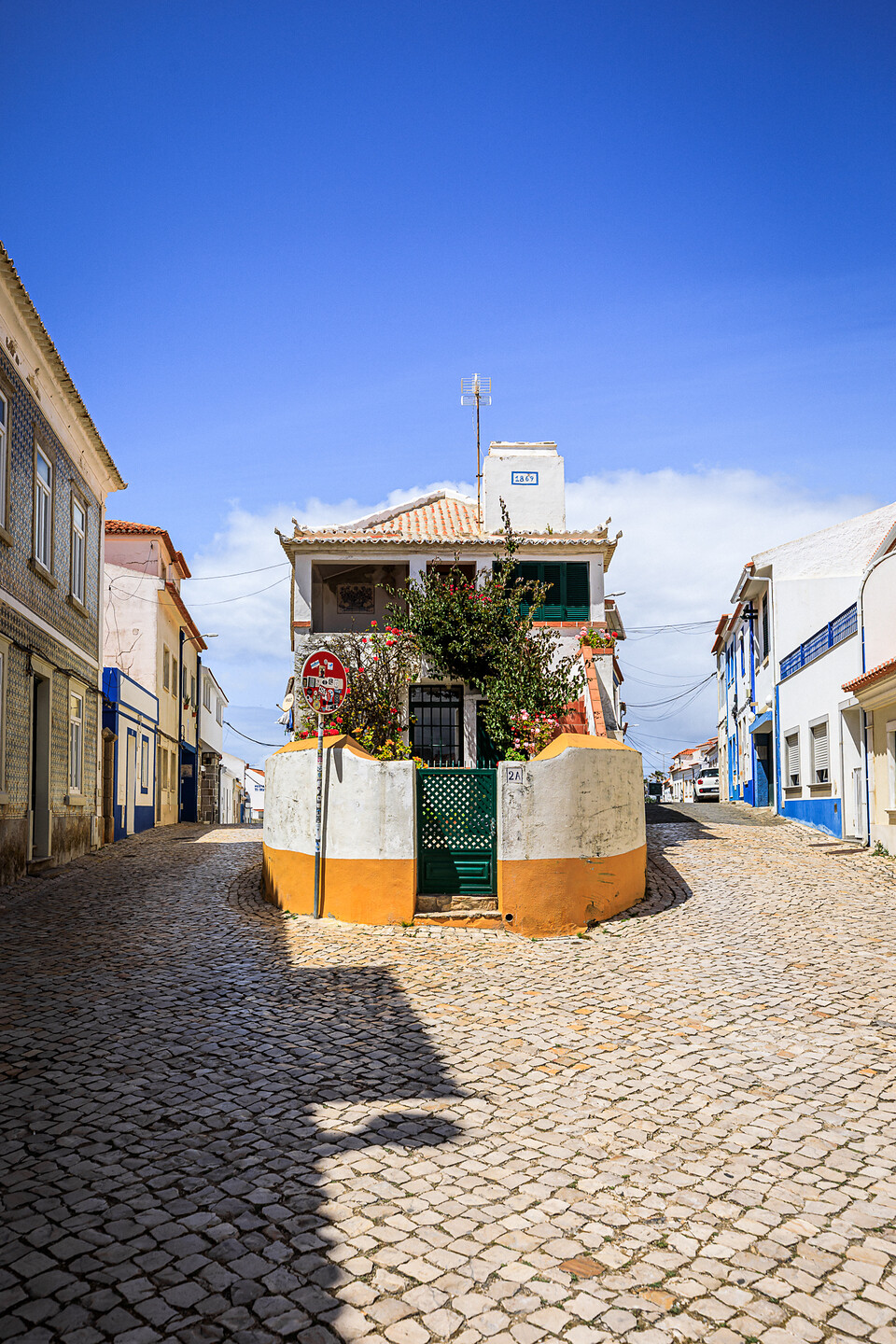 Une maison blanche datant de 1869 au 2A, à l'intersection de 2 rues pavées de Ericeira au Portugal. Un panneau de signalisation couvert d'autocollants.