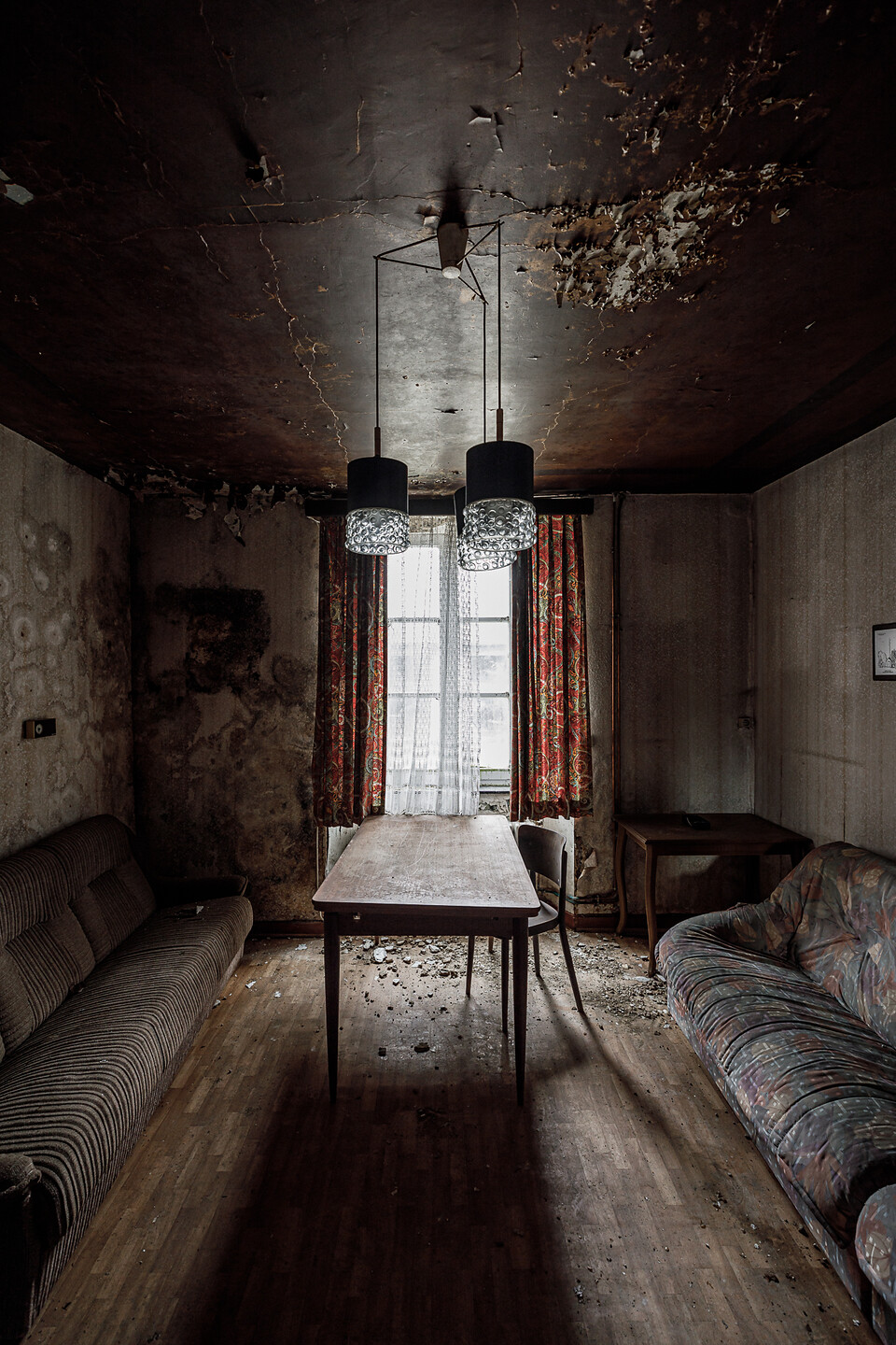 Pièce de vie au plafond marron décrépi, son lustre moderne, ses murs humides et ses canapés sentant le moisi ...