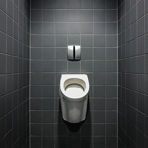 Un urinoir adossé à un mur de carrelages gris antracites...