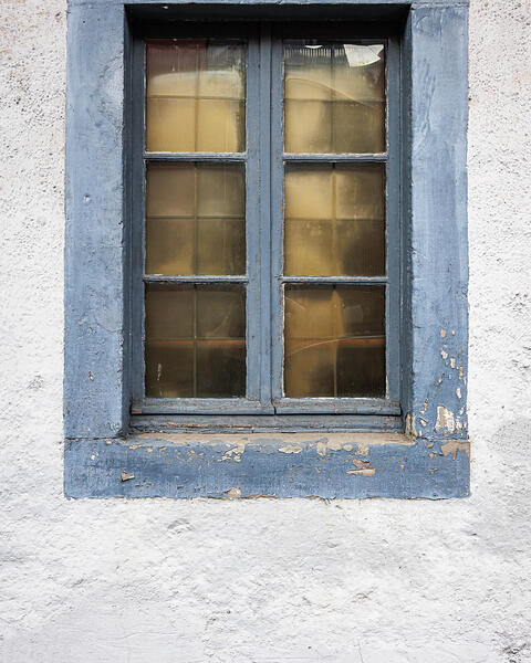 Plein cadre sur une fenêtre aux vitres jaunies et son encadrement peint en bleu sur un mur blanc.