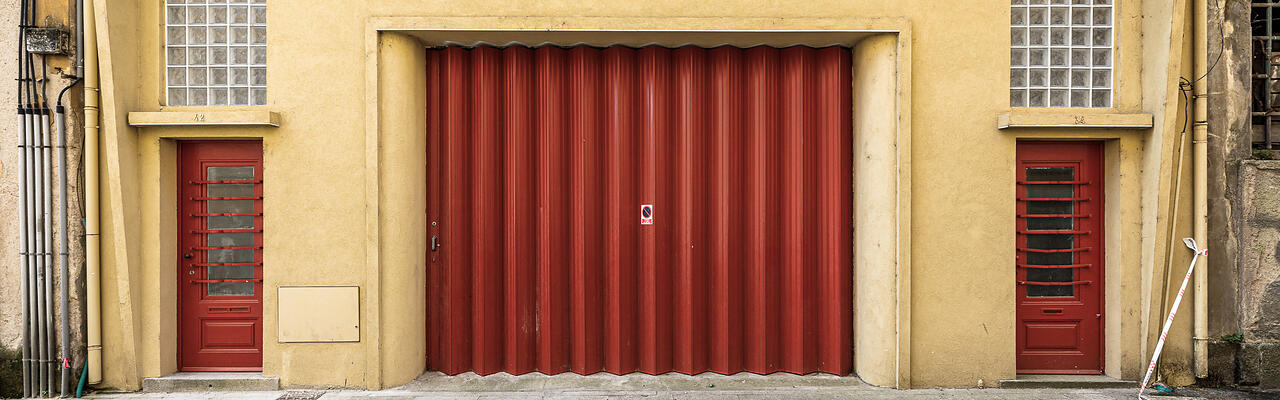 Façade ocre à Vila Nova de Gaia, avec une grande porte industrielle rouge plissée et deux portes latérales.