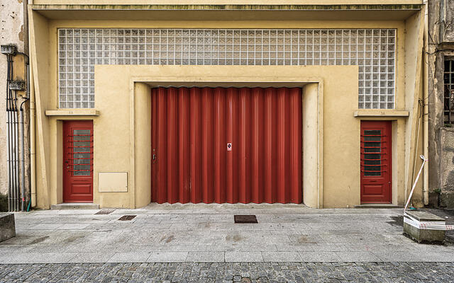 Façade ocre à Vila Nova de Gaia, avec une grande porte industrielle rouge plissée et deux portes latérales.