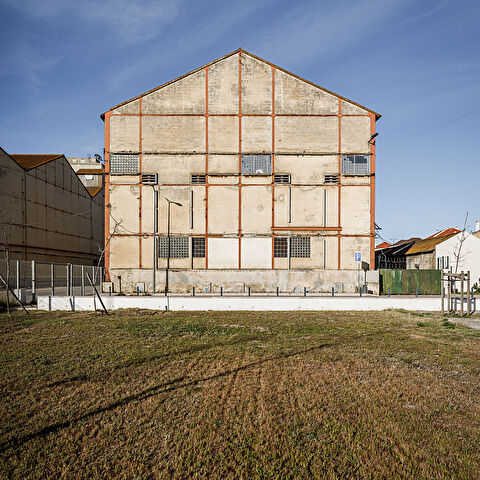 Bâtiment industriel (Companhia União Fabril) en béton avec des structures métalliques rouges, des fenêtres grillagées et sous un ciel bleu.