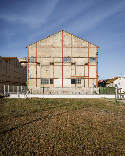 Bâtiment industriel (Companhia União Fabril) en béton avec des structures métalliques rouges, des fenêtres grillagées et sous un ciel bleu.