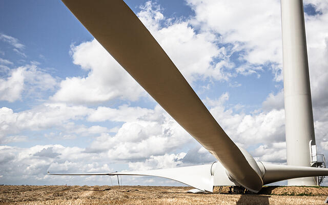 Gros plan d'une pale d'éolienne blanche gisant dans un champ de chaume à Marbais en Belgique, avec une partie de la tour visible et un ciel bleu nuageux en arrière-plan.