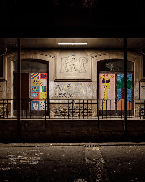Entrée de deux portes colorées: une avec dessins (smiley, arc-en-ciel) et l'autre une girafe, graffitis (FTP, NLP LERNO) sur les murs. Photo de nuit