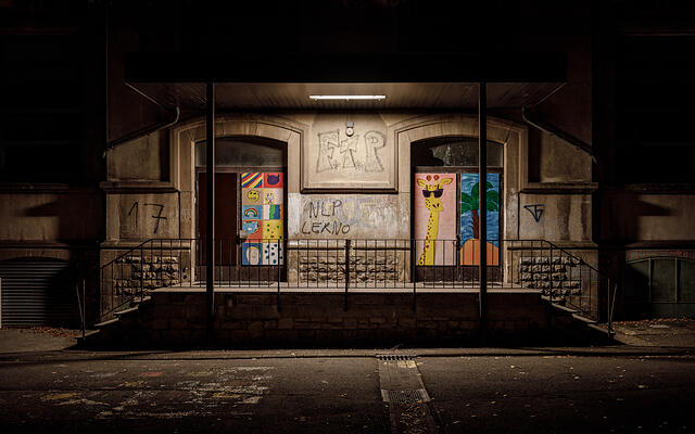 Entrée de deux portes colorées: une avec dessins (smiley, arc-en-ciel) et l'autre une girafe, graffitis (FTP, NLP LERNO) sur les murs. Photo de nuit.