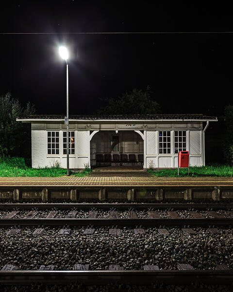 Vue nocturne de face du quai de la gare de Betzdorf, illuminé par un lampadaire puissant au premier plan face aux voies ferrées.