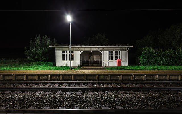 Vue nocturne de face du quai de la gare de Betzdorf, illuminé par un lampadaire puissant au premier plan face aux voies ferrées.