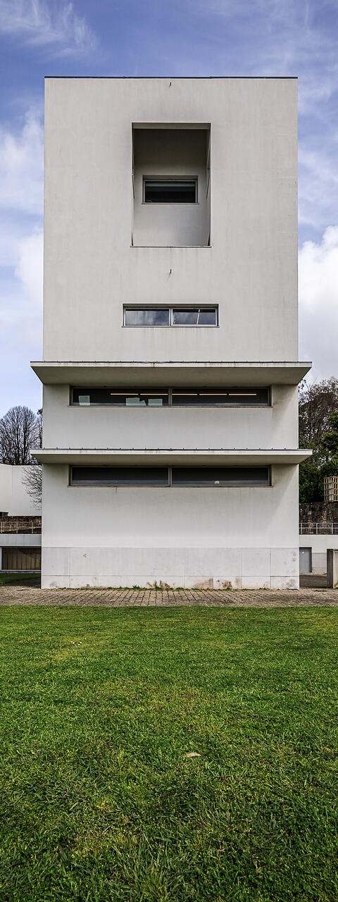 Façade côté rue de la 'Torre H' aux ouvertures géométriques et fenêtres en longueur, s'élevant derrière une pelouse verte. (Massarelos, Porto, Portugal)