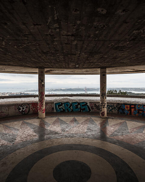Intérieur du Miradouro de Monsanto montrant des colonnes couvertes de street art, un sol en mosaïque étoilée et une vue sur le pont du 25 Avril.