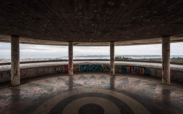 Intérieur du Miradouro de Monsanto montrant des colonnes couvertes de street art, un sol en mosaïque étoilée et une vue sur le pont du 25 Avril.