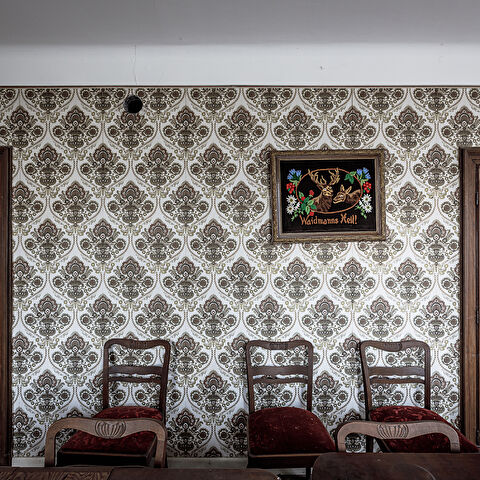 Austère salle à manger meublée de chaises aux coussins de velours rouge. Avec pour seule décoration un cadre illustré 'Waidmanns Heil!' ...