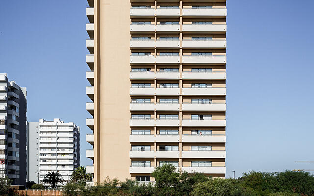 Tour de l'hôtel Wyndham s'élevant derrière un terrain vague d'herbes sèches, vue frontale sous un grand ciel bleu. (Alvor, Portugal)